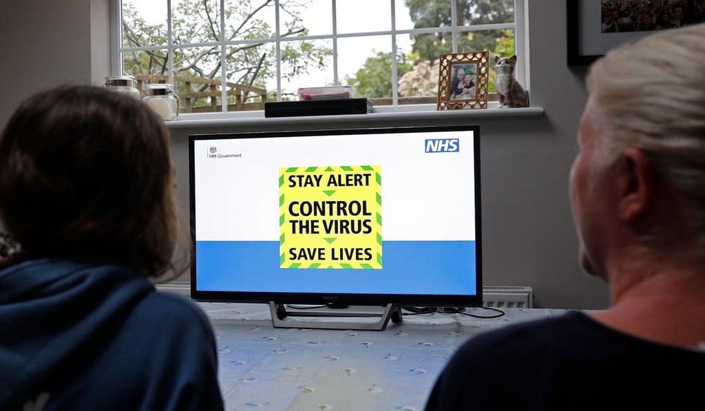 The government's new catchphrase is displayed on screen as a family gather around the television in London to watch Britain's Prime Minister Boris Johnson give a televised message to the nation on Sunday. Photo: AFP