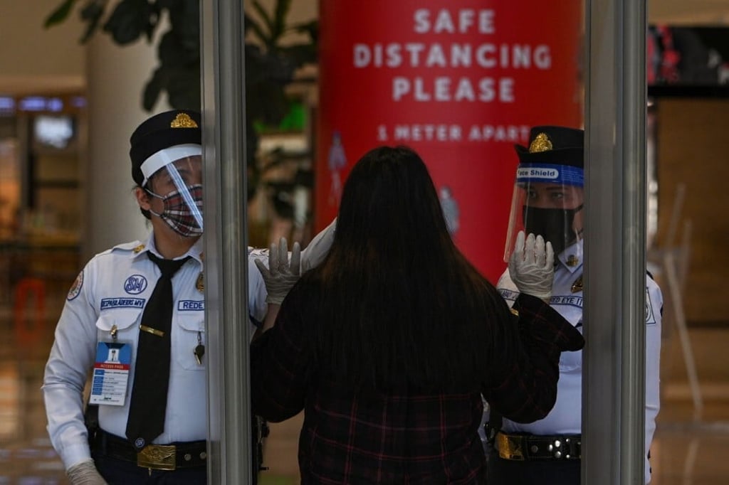 A security guard takes the temperature of a shopper at the entrance of a shopping centre in Manila on May 16, 2020. Photo: AFP