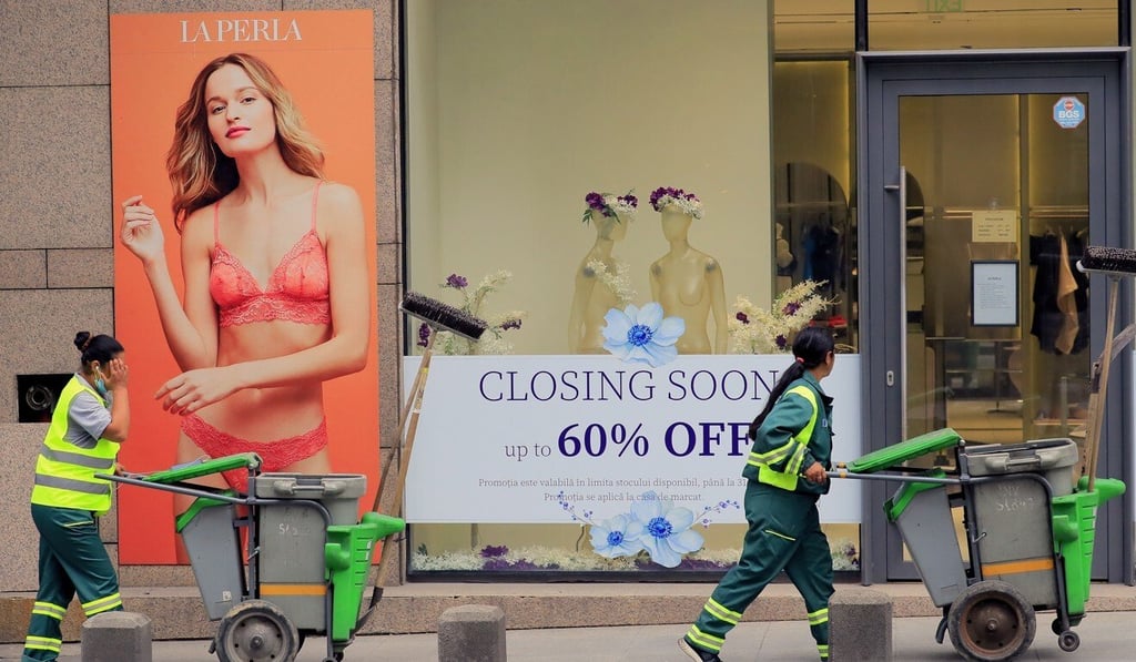 Municipal workers pass the window of a luxury fashion store announcing a closing-down sale in Bucharest, Romania, on May 14. Photo: EPA-EFE