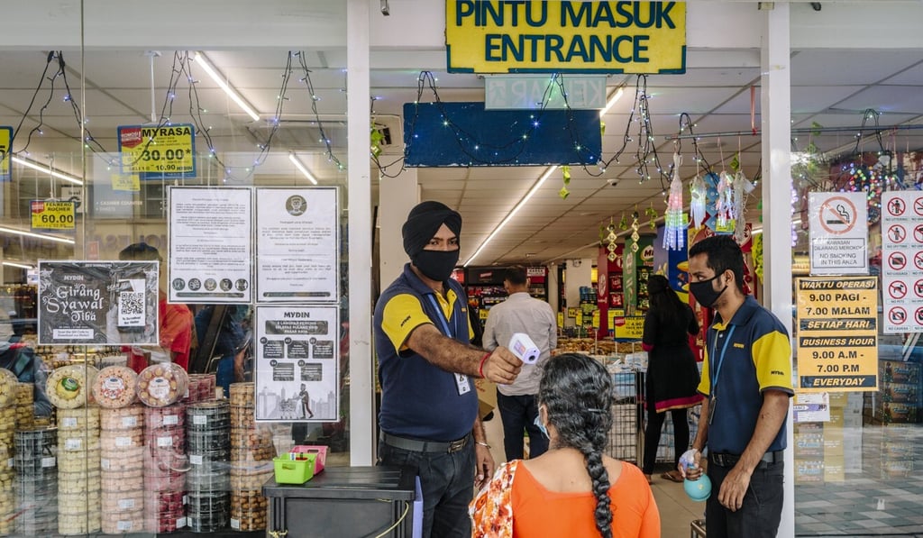 A worker wearing a protective mask checks a customer’s temperature at an entrance to a grocery store in Kuala Lumpur last month. Photo: Bloomberg A worker wearing a protective mask checks a customer’s temperature at an entrance to a grocery store in Kuala Lumpur last month. Photo: Bloomberg