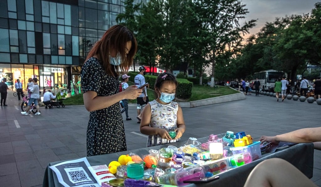 A woman buys a toy for a girl from a street vendor in Beijing. City municipal authorities have made it clear they will not be re-embracing street vendors as a means of protecting employment. Photo: EPA-EFE