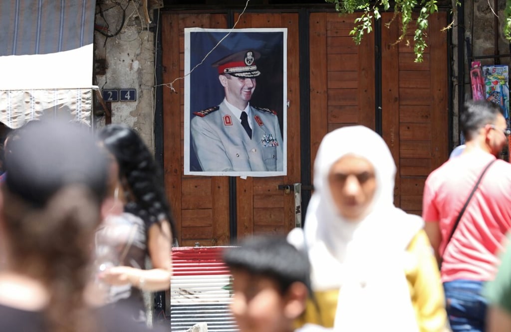 Syrians walk in old Damascus in front of a portrait of Syrian President Bashar al-Assad, on June 16, 2020. Photo: AFP