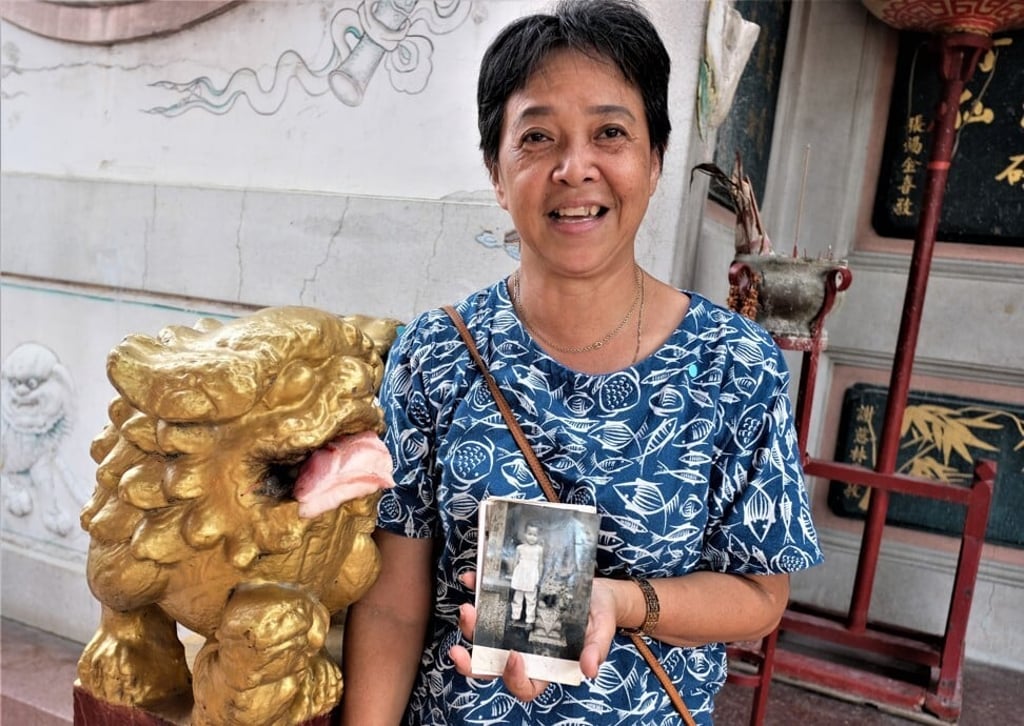 Wanphen Ploysisuay, an ethnic Chinese woman whose family has been caretakers of the shrine for generations, at the temple next to a guardian lion with a picture of herself as a little girl at the same spot. Photo: Tibor Krausz