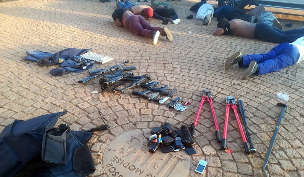 Confiscated arms and ammunition, foreground, and arrested suspects, background, lay face-down at a church in Zuurbekom. Photo: South African Police Services via AP