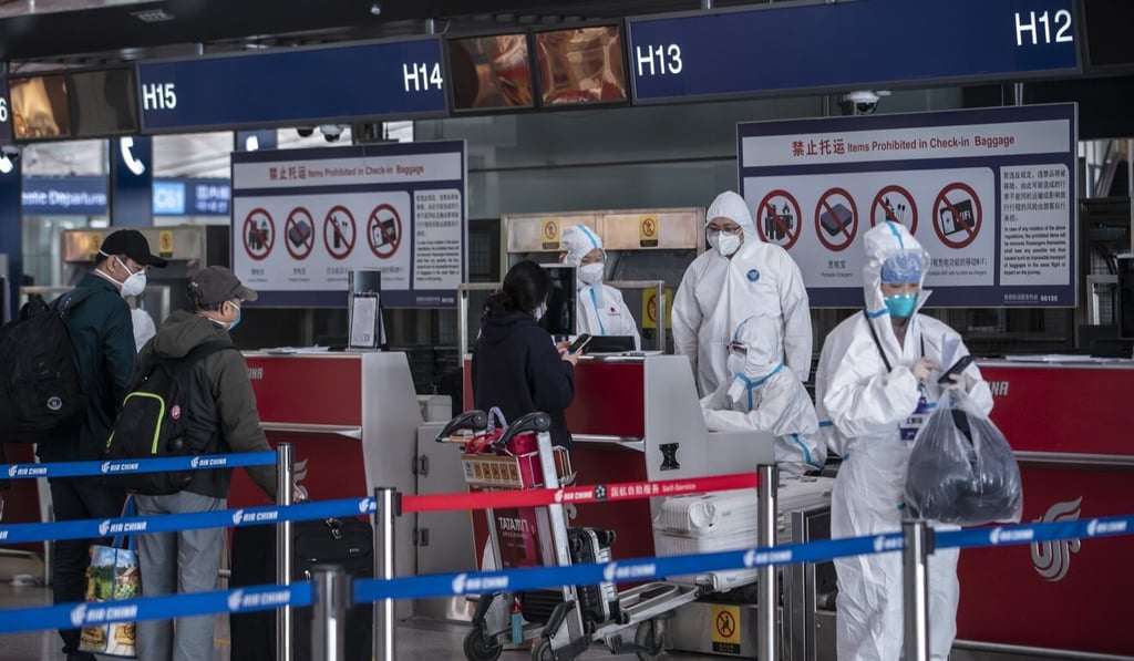 Airport employees wearing full-body protective suits assist inbound passengers at the Capital International Airport in Beijing on March 18. Photo: Bloomberg Airport employees wearing full-body protective suits assist inbound passengers at the Capital International Airport in Beijing on March 18. Photo: Bloomberg