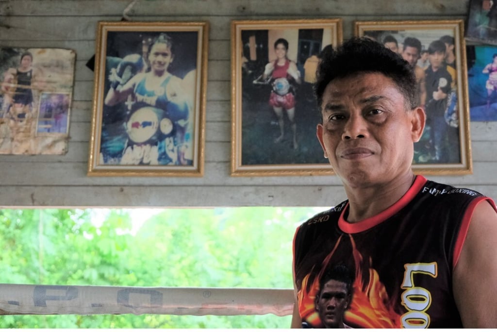 Nopparit Yoohanngoh, a Thai Muslim man who has trained all of his 16 children in Muay Thai, stands in front of photographs of some of his daughters at his gym in Bangkok. Photo: Tibor Krausz