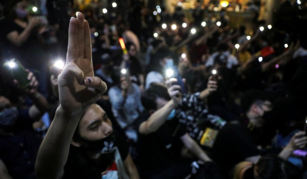 A pro-democracy protester flashes a salute as others use mobile phones as torchlights during a protest demanding the resignation of Prayuth Chan-ocha in Bangkok on Monday. Photo: Reuters
