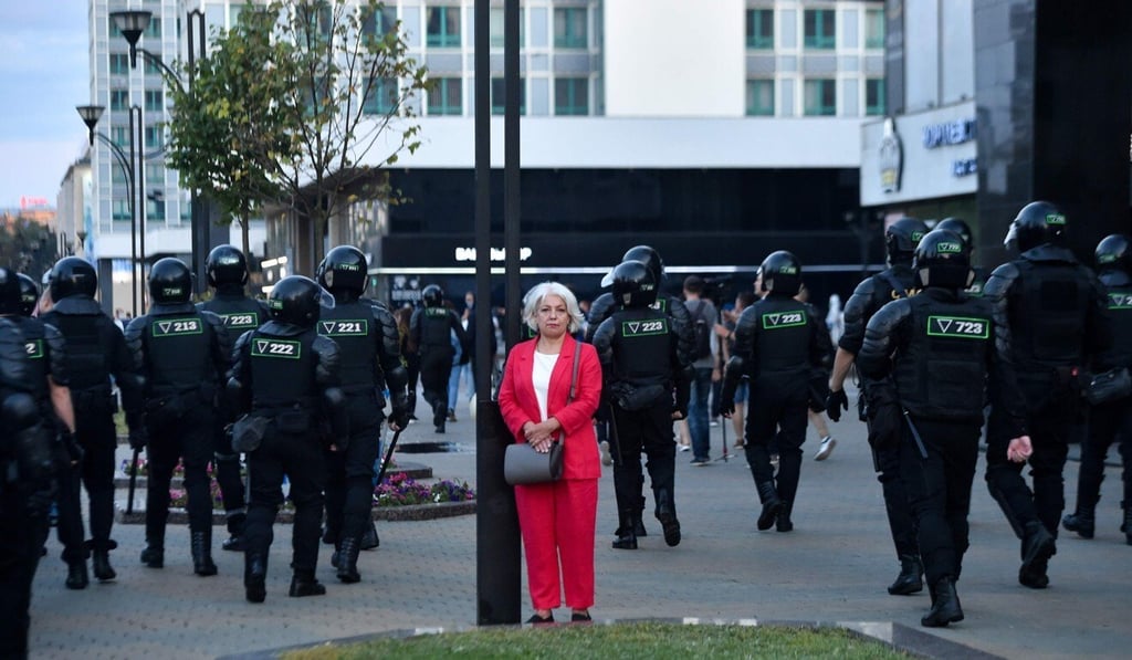 A woman stands by a lamp post as riot police move along a street during a protest on Monday. Photo: AFP A woman stands by a lamp post as riot police move along a street during a protest on Monday. Photo: AFP