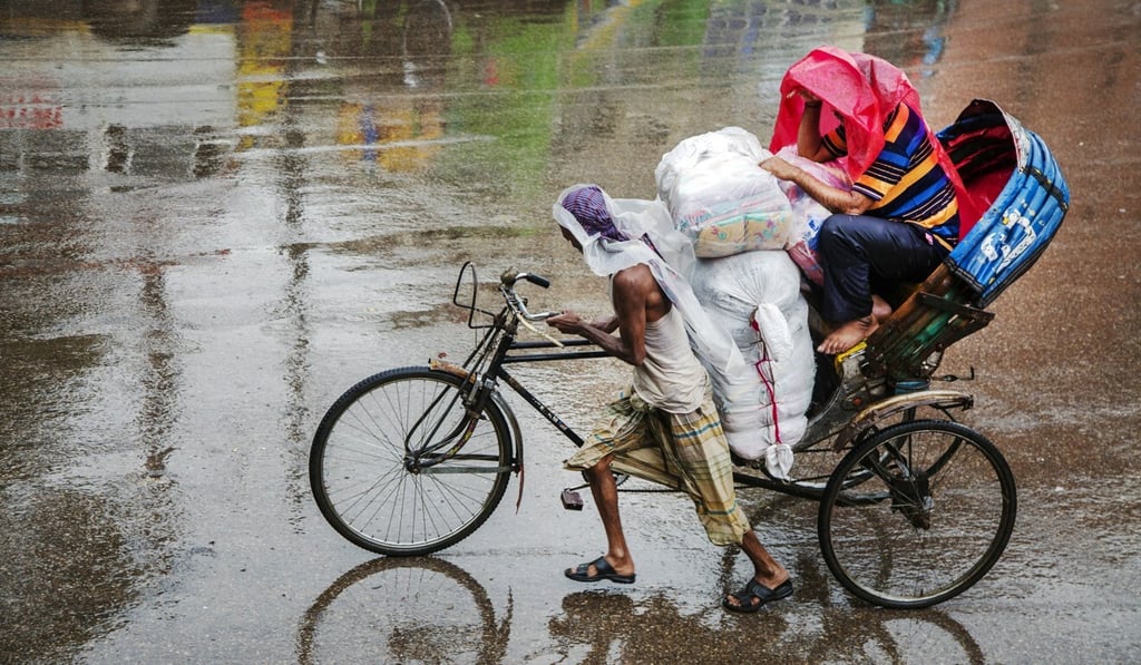 A rickshaw puller with a passenger covering himself during rain in Dhaka. Photo: EPA