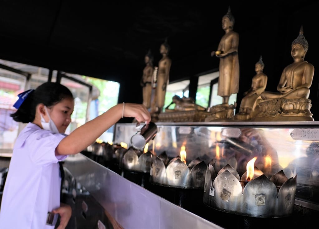A young worshipper at Wat Soi Thong Buddhist temple in Bangkok pours oil on flames burning before Buddha statues so as to make merit. Photo: Tibor Krausz