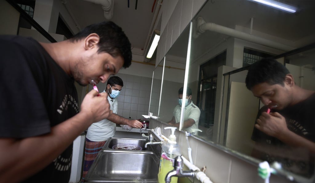 A migrant worker brushes his teeth as another prepares to cook at a wash area in their dormitory room in Singapore on August 18. Photo: EPA