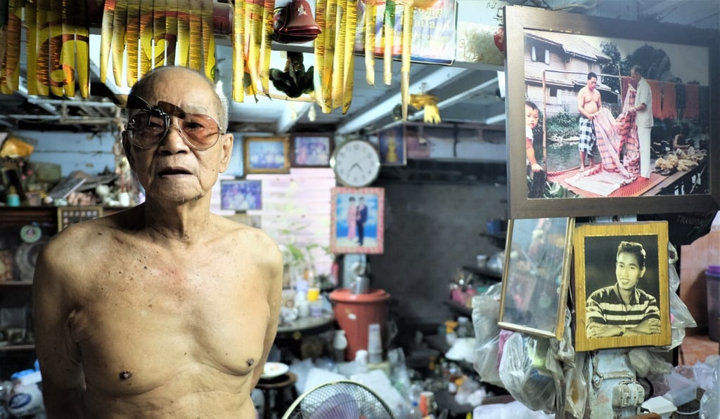 Manasnan Benjarongchinda, a Chinese-Thai silk maker, stands in his simple home beside a picture from around 1960 showing American businessman Jim Thompson outside the same house in Baan Khrua. Photo: Tibor Krausz