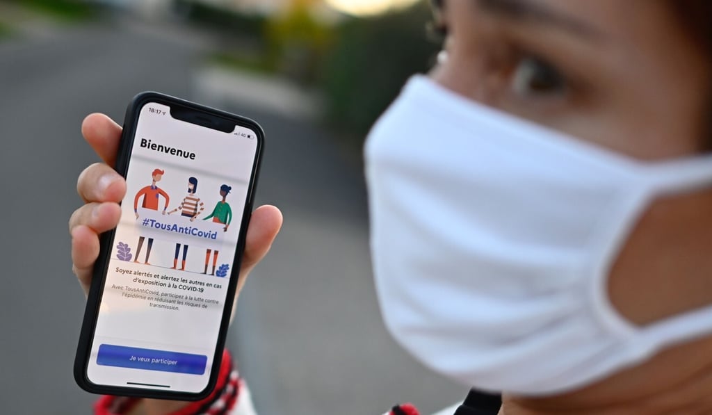 A French woman wearing a face mask holds a smartphone showing the new antivirus app. Photo: AFP