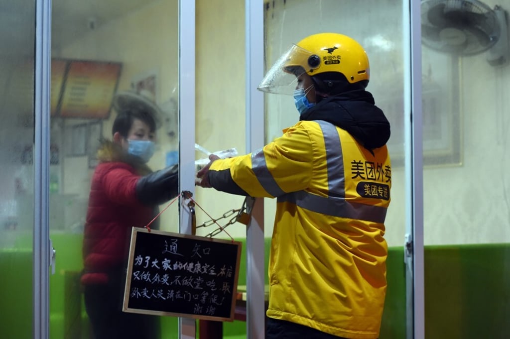 A Meituan delivery man carefully passes food through chained doors during coronavirus-induced lockdowns in Hefei, Anhui province, earlier this year. Photo: Xinhua