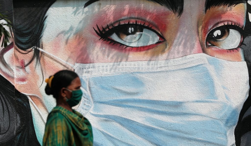 A woman wearing a mask walks past graffiti of a woman wearing a mask in Mumbai on October 23. Photo: Reuters