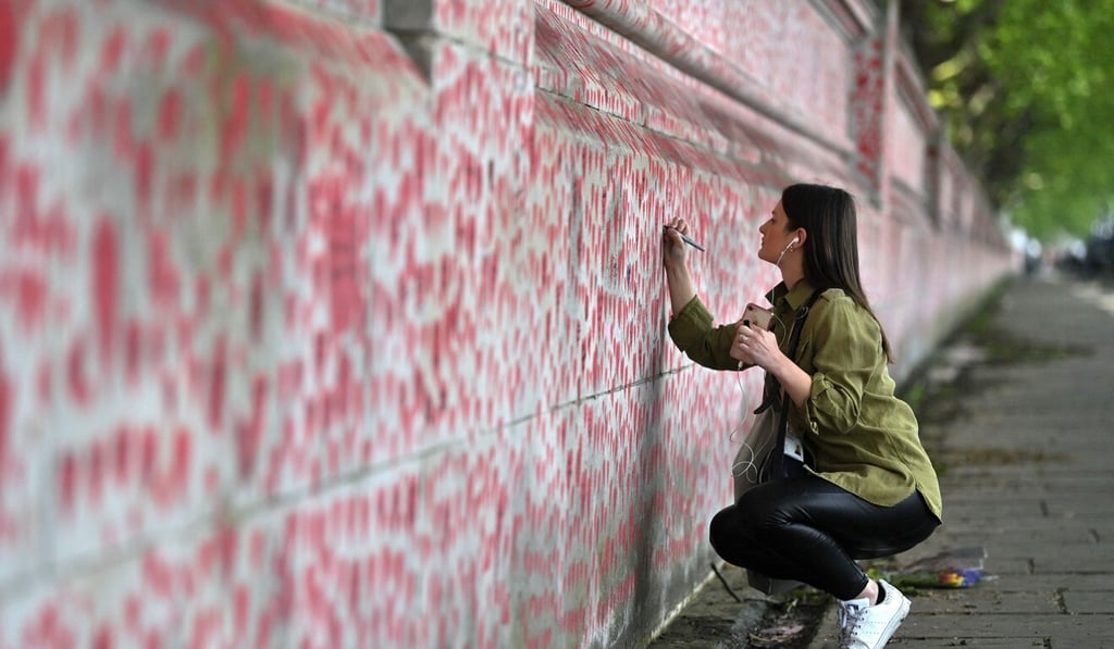 A woman writes a message on a heart painted on the National Covid Memorial Wall in London on Friday. Britain has Europe’s highest virus-related death toll at more than 127,500. Photo: AFP
