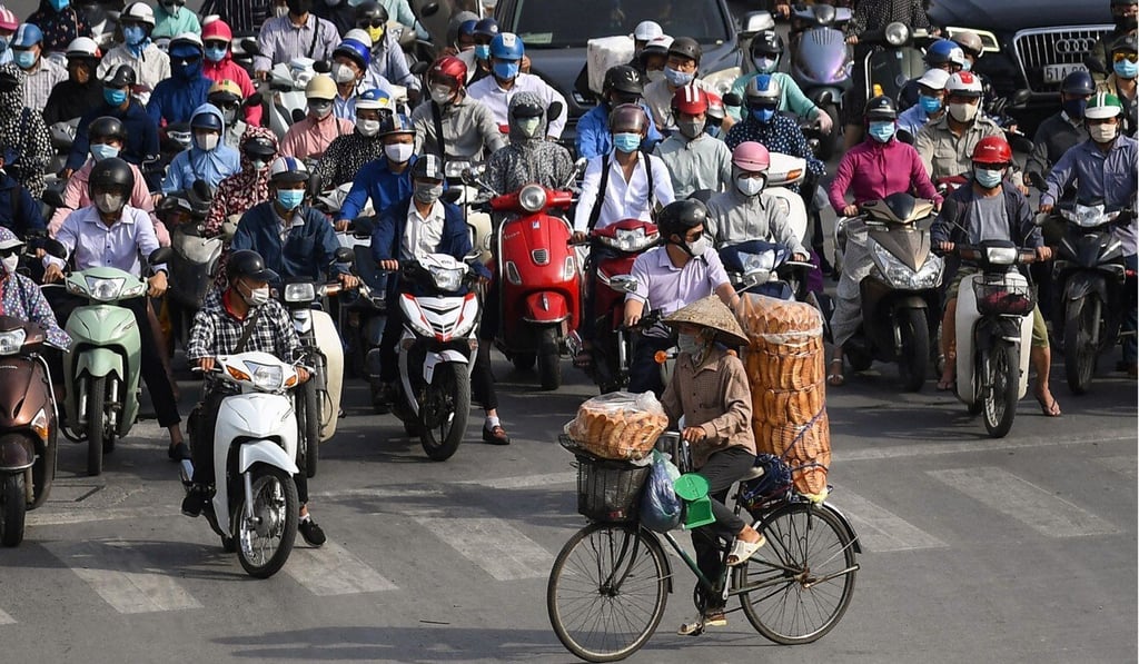 A bread seller cycles past motorists waiting at a traffic light in Hanoi. Many Vietnamese still shop at family-run stores and traditional wet markets. Photo: AFP