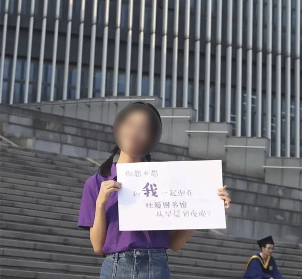A woman poses with a sign that reads “Do you want to live at the library with me, from morning till night?” at Nanjing University. Photo: Weibo