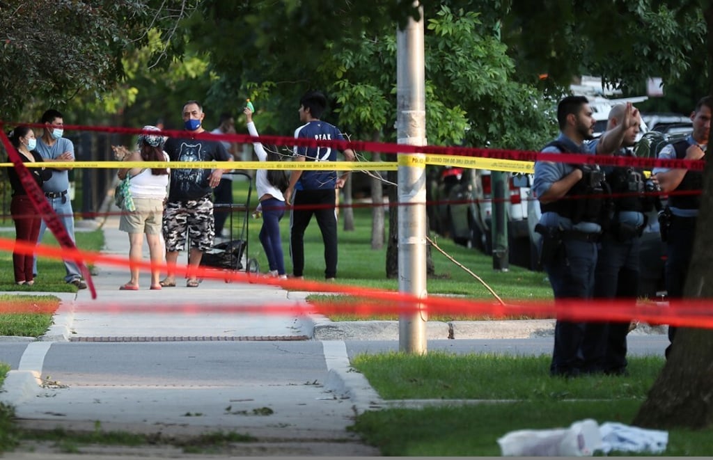 A child raises a toy gun in the air as police officers investigate the scene of a fatal shooting in Chicago. Photo: Chicago Tribune / TNS