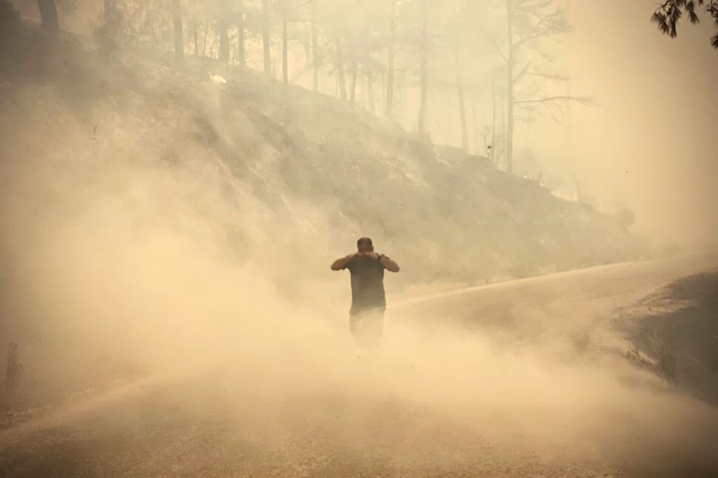 A pedestrian walks through the smoke as a massive fire engulfed a Mediterranean resort region on Turkey’s southern coast near the town of Manavgat on Friday. Photo: AFP