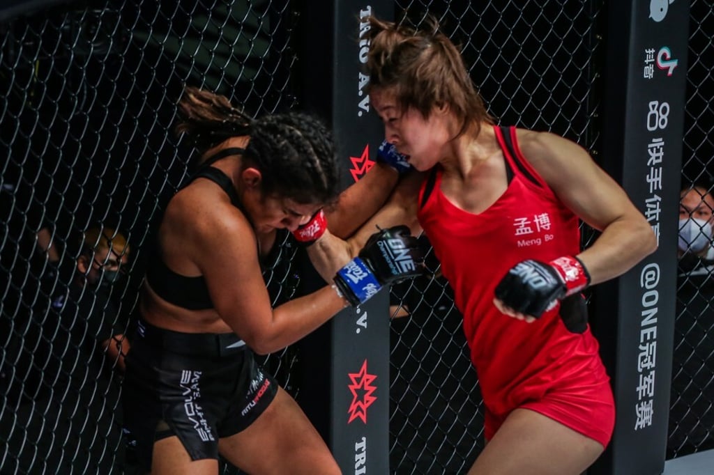 Meng Bo lands a punch on Ritu Phogat against the cage at ONE: Empower.