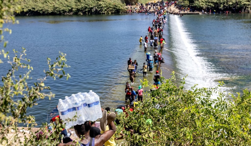 Migrants walk across the Rio Grande carrying food and other supplies back to a makeshift encampment under the International Bridge between Del Rio, Texas, and Mexico on Friday. Photo: AFP