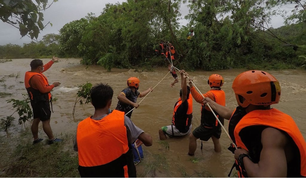 People are helped across a flooded river during Tropical Storm Kompasu in the Philippines. Photo: AFP