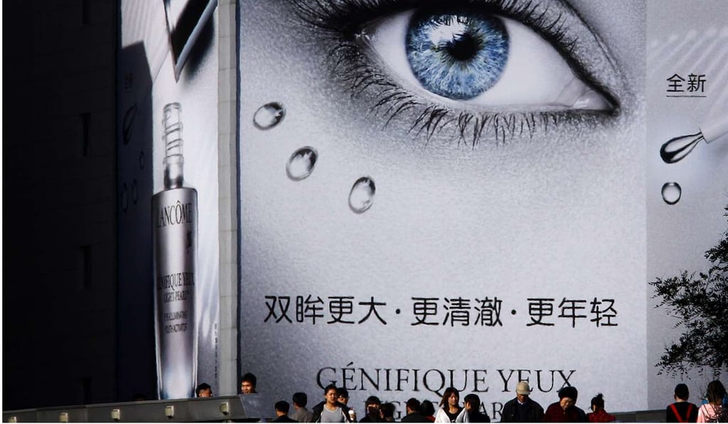 Shoppers walk across a pedestrian bridge in front of a giant billboard for French luxury cosmetics house Lancome in central Beijing. Photo: Reuters