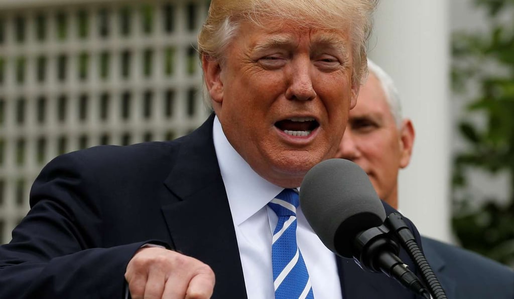 US President Donald Trump (L), flanked by Vice President Mike Pence (R), delivers remarks to members of the Independent Community Bankers Association in the Kennedy Garden at the White House as protesters march around the country. Photo: Reuters