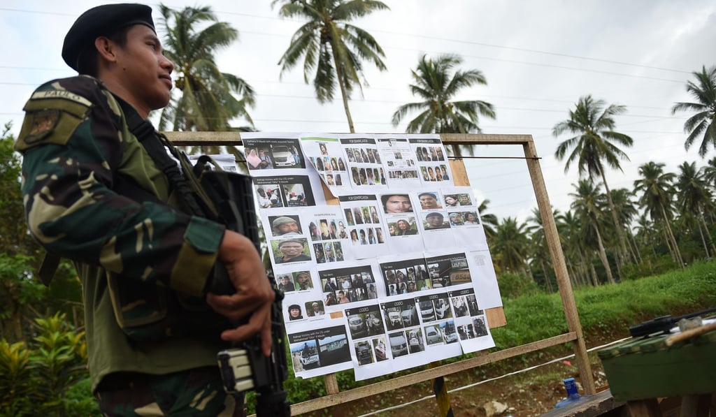 A Philippine soldier stands guard next to images of wanted militants displayed along a highway where they set up a check point, in Balo-i, Mindanao, on May 29. Photo: AFP