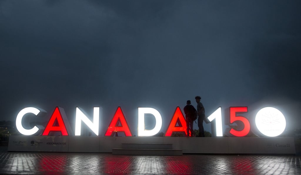 Tourists stand near an illuminated Canada 150 sign in Niagara Falls, Ontario. Photo: Bloomberg