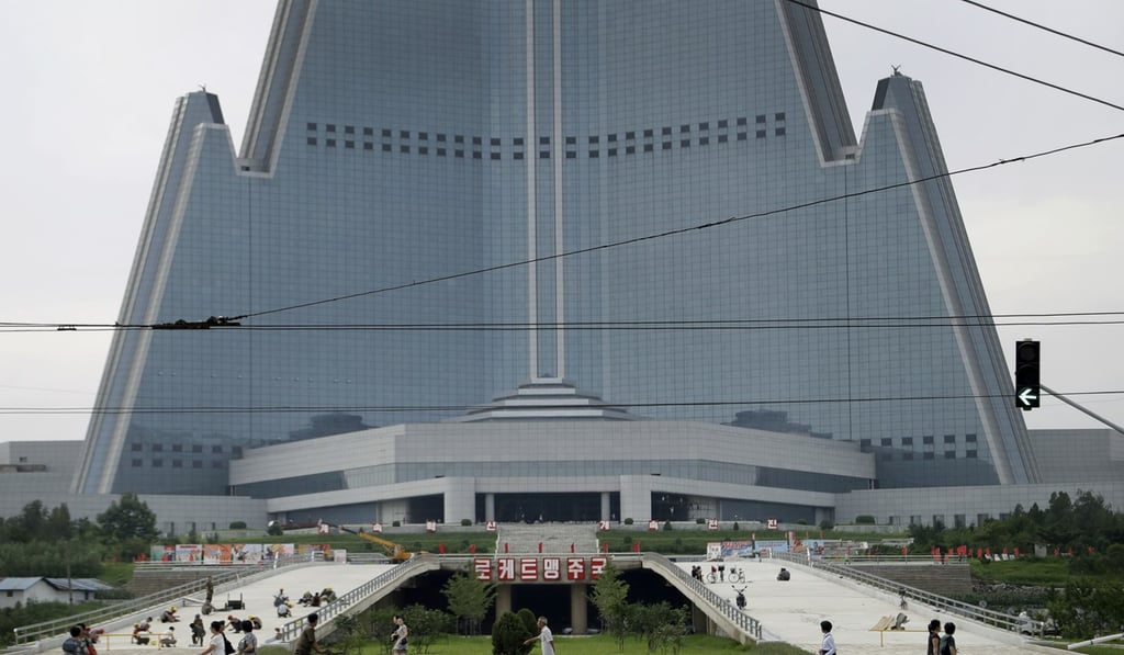 People walk past the 105-storey pyramid shaped Ryugyong Hotel where men are seen working on a driveway leading up into its entrance in Pyongyang. Photo: AP People walk past the 105-storey pyramid shaped Ryugyong Hotel where men are seen working on a driveway leading up into its entrance in Pyongyang. Photo: AP