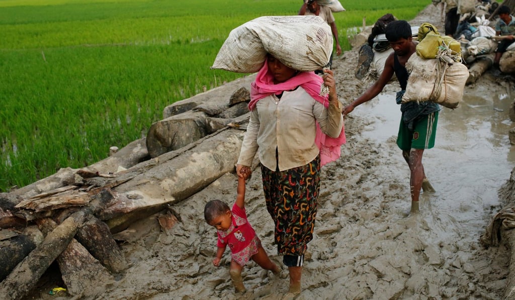 A Rohingya refugee woman holds her child as they walk on the muddy path after crossing into Bangladesh. Photo: Reuters