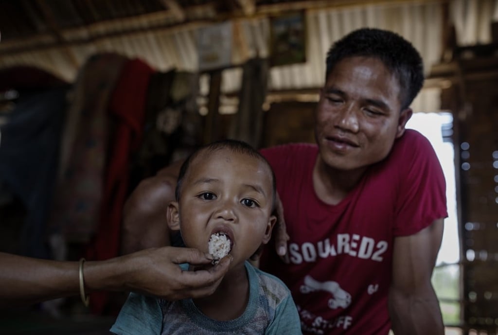 Farmer Khemtay Keolabao with his son by his second wife, Chien, in their stilt home in the village.