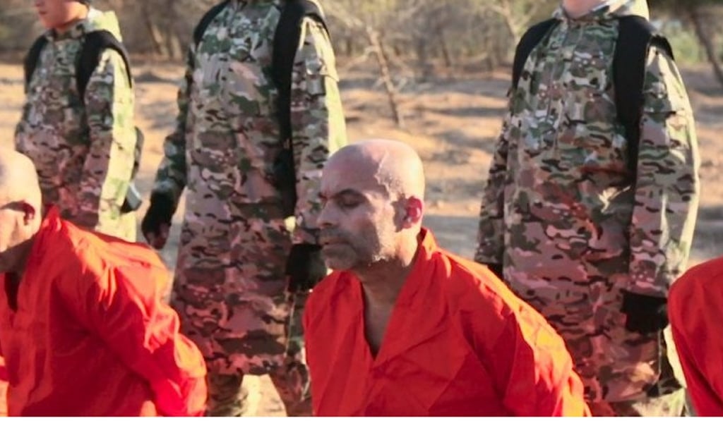 A boy believed to be Jojo Jones (standing, left), then 11, is seen in an Islamic State execution video, before shooting dead the man kneeling in front of him. Photo: Supplied