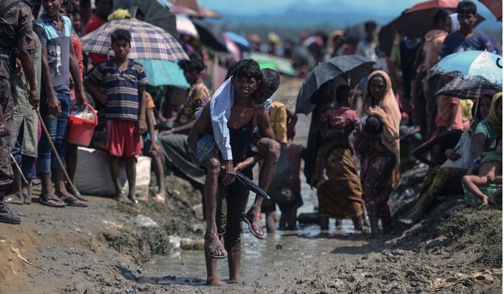 A Rohingya refugee carries an old man on the Bangladesh side of the border with Myanmar, after crossing the Naf River on October 17. Photo: AFP