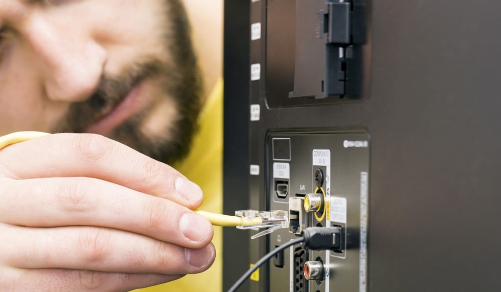A technician hooks up an internet cable to a TV.