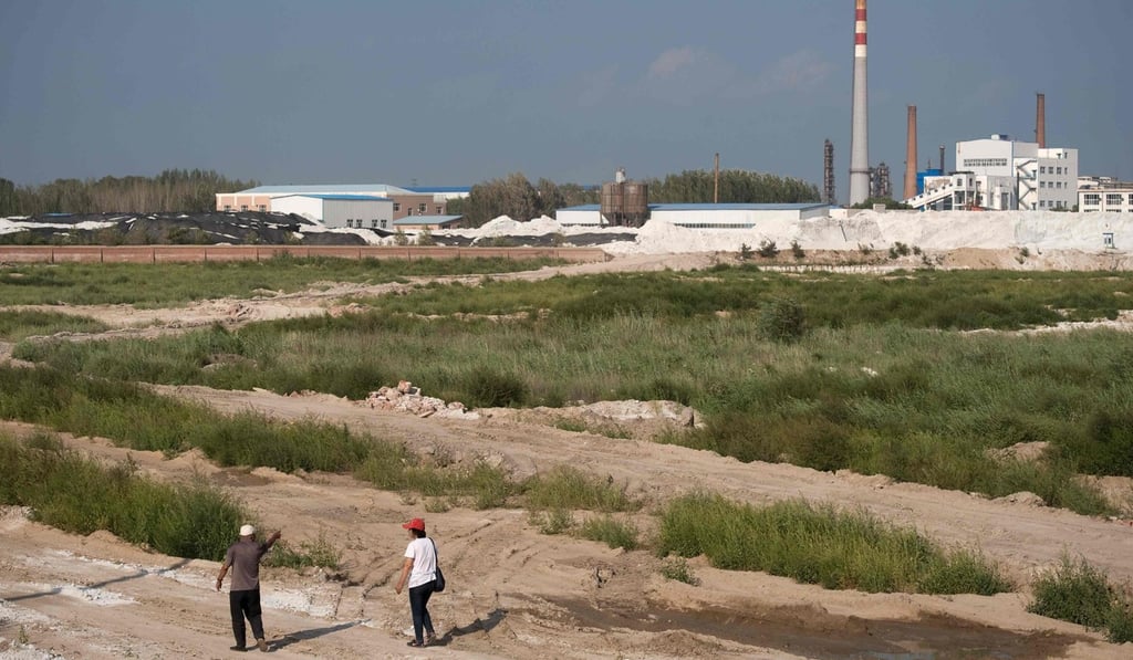 Two members of the “Senior Citizen Environmental Protection Team” walk on farmland that was polluted by the Qihua chemical plant (right) in Yushutun. Photo: AFP
