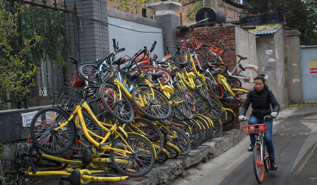 A woman rides past a pile of shared bikes in Beijing. Photo: Reuters