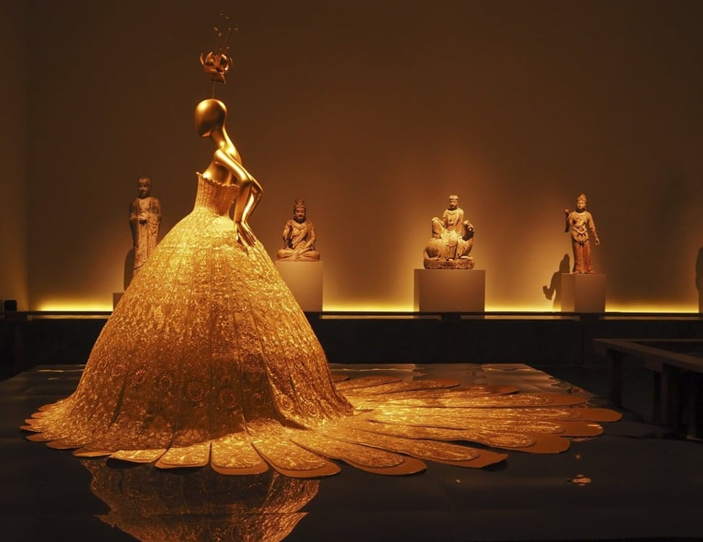 At The Metropolitan Museum of Arts ‘China: Through The Looking Glass’ exhibit, the juxtaposition of a modern day Guo Pei gold gown featuring a traditionally Western profile and ancient Buddhist sculptures provides fresh insight into both while creating a dramatically interesting East meets West space. Photo: Vern Yip