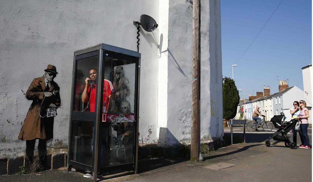 A man stands in a phone box next to graffiti by street artist Banksy spoofing government spying scandals. Photo: Reuters