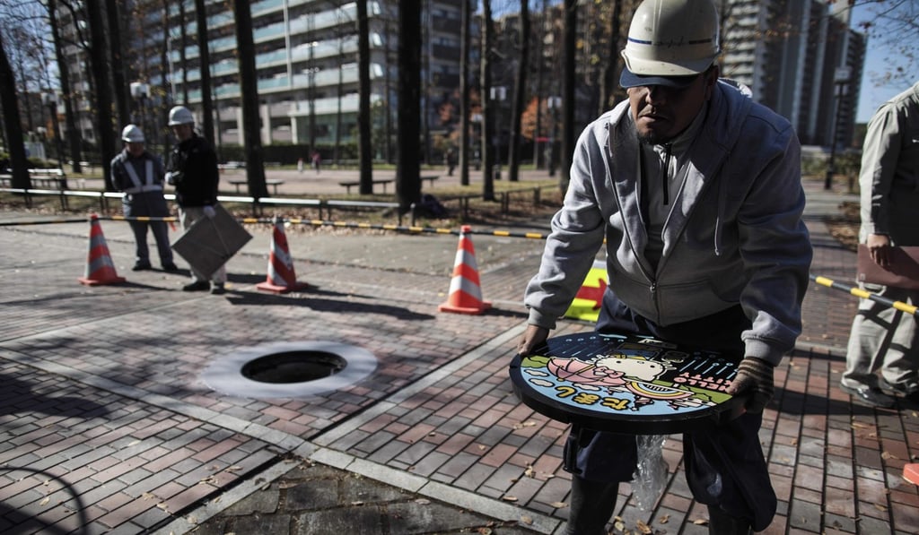 A worker installing a Hello Kitty manhole cover in Tama Chuo park in Tama city, Tokyo prefecture. Photo: AFP