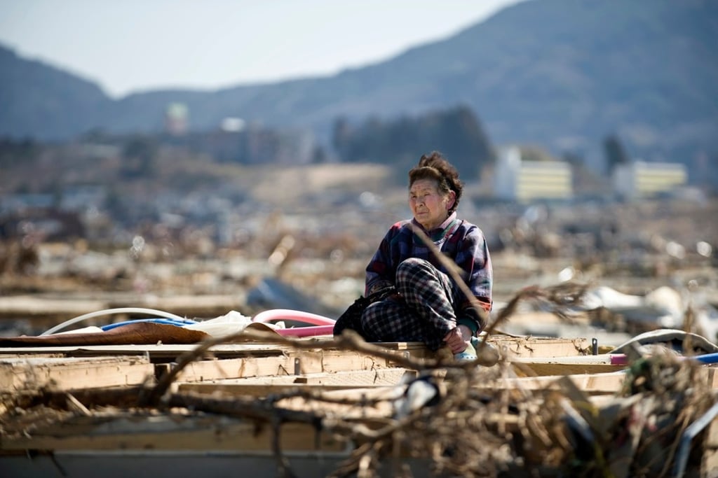 A tsunami survivor sits on the flattened remains of her former home. Picture: Rob Gilhooly