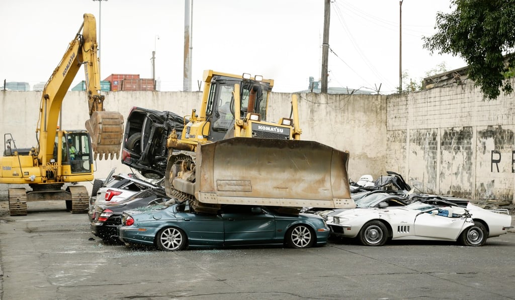 A bulldozer crushes smuggled luxury cars. Photo: EPA