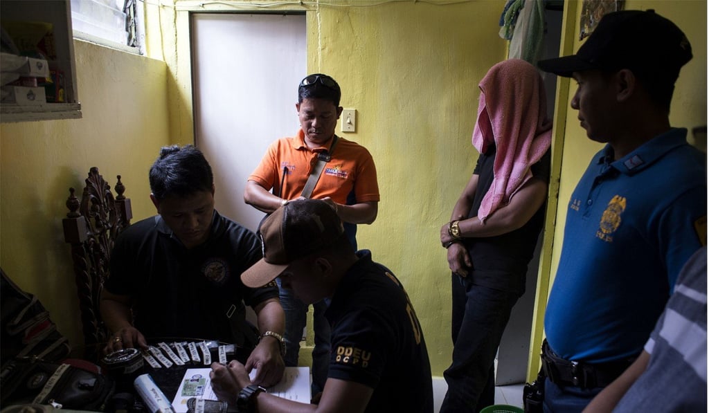 Philippines police investigate after a drug raid as a suspect (second from right) covers his face. Photo: AFP