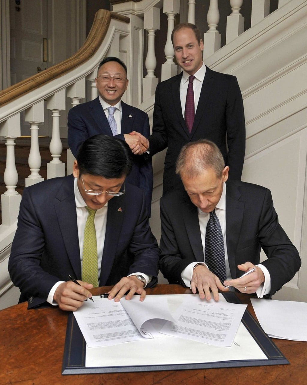 Britain's Prince William (rear R) shakes hands with Yuan Yafei, the chairman of Chinese corporation Sanpower, as Yue Lei (L) and Nick Booth, CE of The Royal Foundation, sign a memorandum of understanding for the United For Wildlife charity, at Kensington Palace in London, Britain October 21, 2015. Photo: REUTERS/Nick Ansell