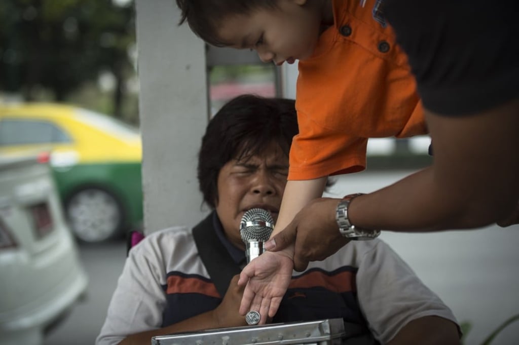 Guided by an adult’s hand, a child makes a donation to blind singer Yupin Boonchuen, 50, as she performs on a Bangkok street. Photo: AFP