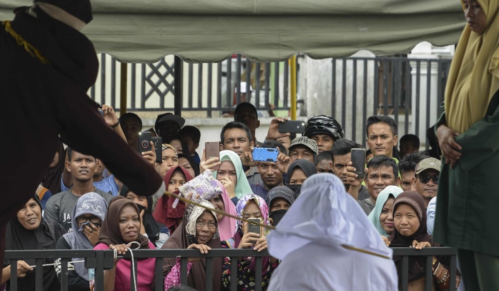 People watch as Tjia Nyuk Hwa, 45, an Indonesian Christian, is publicly flogged outside a mosque in Banda Aceh on February 27, 2018, for playing a children's entertainment game seen as violating Islamic law. Photo: AFP