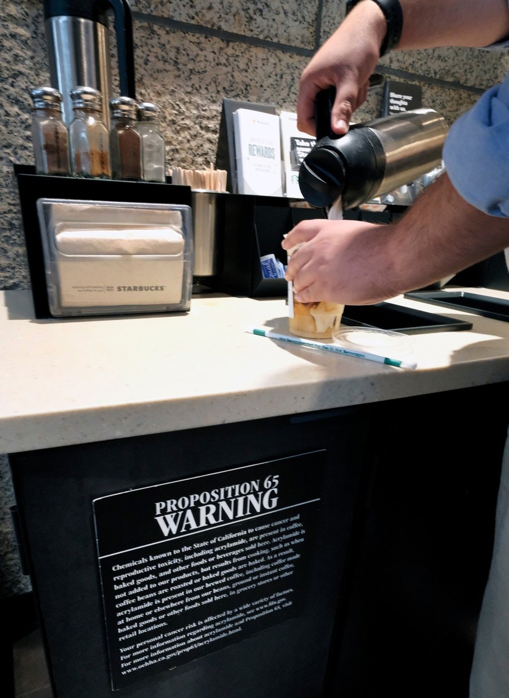 A customer pours milk into coffee near a posted Proposition 65 cancer warning sign at a Starbucks coffee shop in Los Angeles. Photo: AP