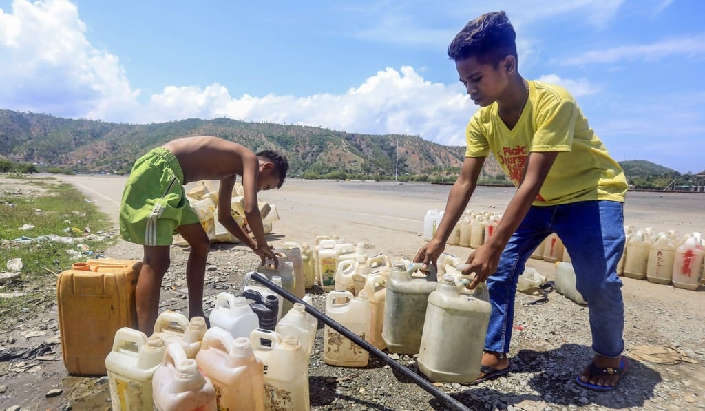 East Timorese boys pour clean water in to plastic containers on a street side in Dili. Photo: EPA